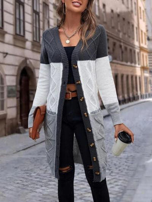 a woman standing on a cobblestone street wearing a gray and white cardigan