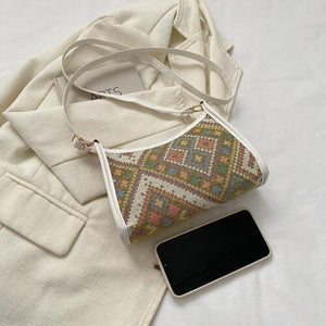 a white purse sitting on top of a bed next to a cell phone