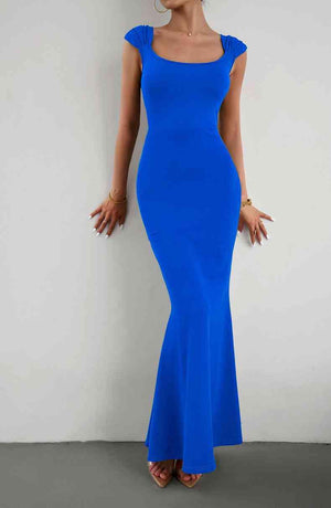 a woman in a blue dress leaning against a wall