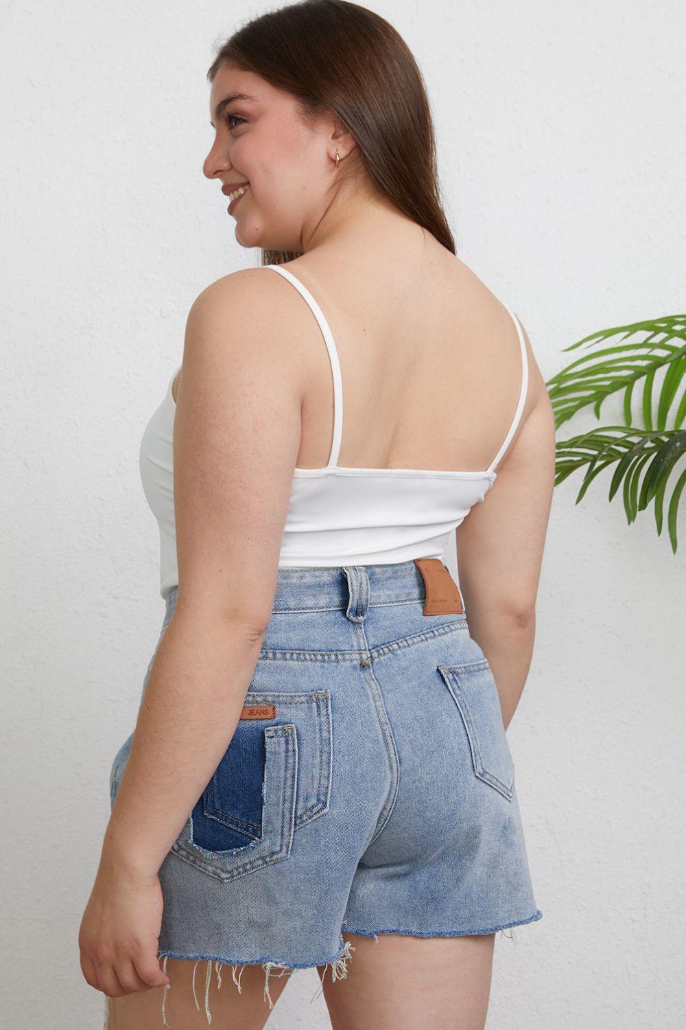 a woman wearing a white tank top and denim shorts