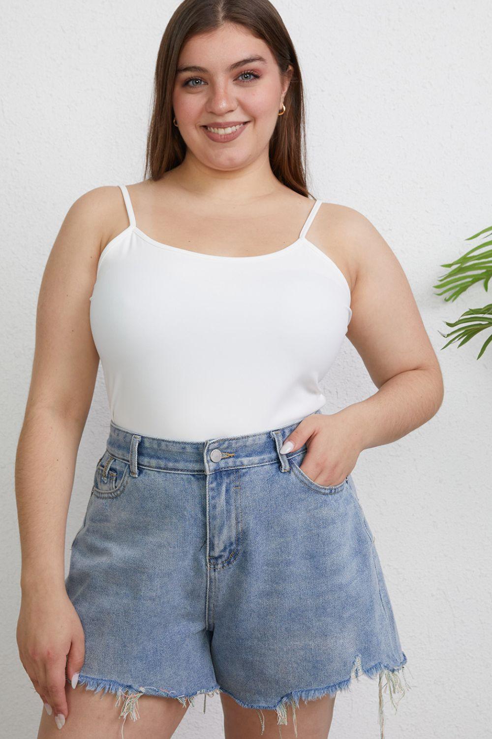 a woman wearing a white tank top and denim shorts