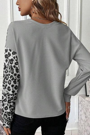 a woman wearing a grey sweater with leopard print sleeves