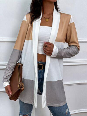 a woman standing against a wall wearing a white and brown cardigan