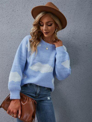 a woman in a blue sweater and hat leaning against a wall