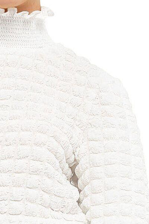 a woman wearing a white sweater with ruffles