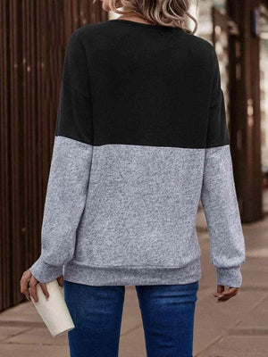 a woman standing on a sidewalk wearing a black and grey sweater
