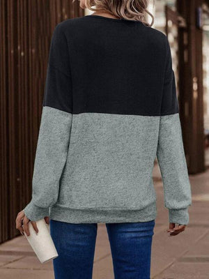 a woman standing on a sidewalk wearing a black and grey sweater