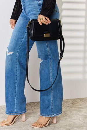 a woman holding a black purse standing next to a wall