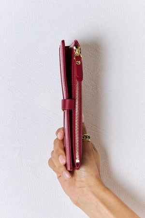 a hand holding a red purse with a gold zipper