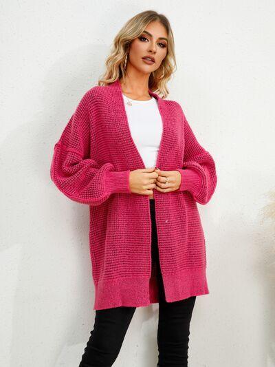 a woman standing in front of a white wall wearing a pink cardigan