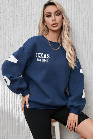 a woman sitting on a stool wearing a texas sweatshirt