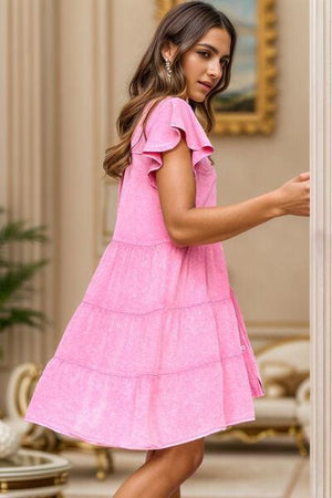 a woman in a pink dress is leaning against a wall