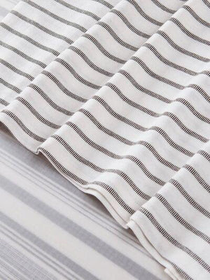 a close up of a bed with a white and gray striped comforter