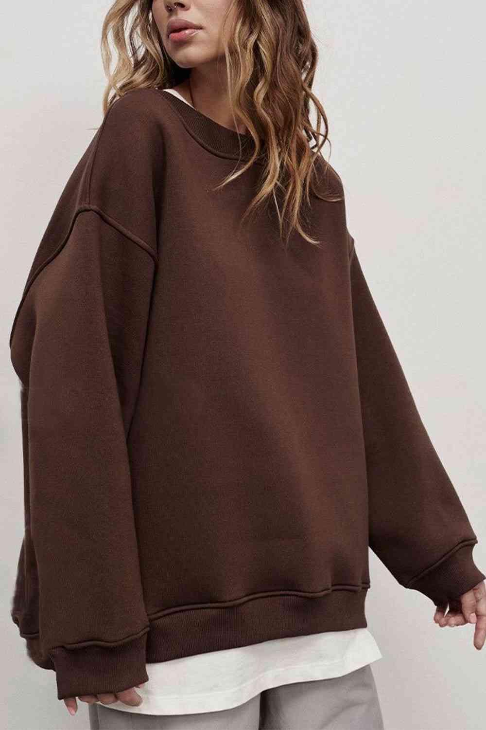 a woman standing in front of a white wall wearing a brown sweatshirt
