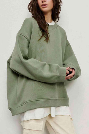 a woman standing in front of a white wall wearing a green sweatshirt