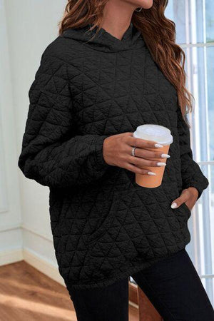 a woman wearing a black quilted hoodie holding a cup of coffee