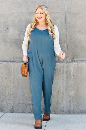 a woman standing in front of a wall wearing a blue jumpsuit