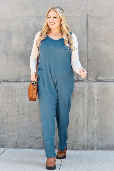 a woman standing in front of a wall wearing a blue jumpsuit