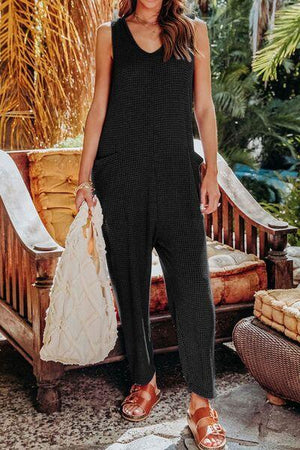 a woman in a black jumpsuit holding a white bag