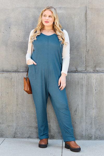 a woman standing in front of a wall wearing a blue jumpsuit