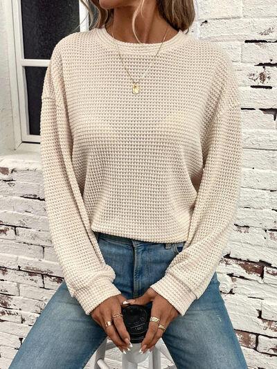 a woman sitting on a stool wearing a white sweater and jeans