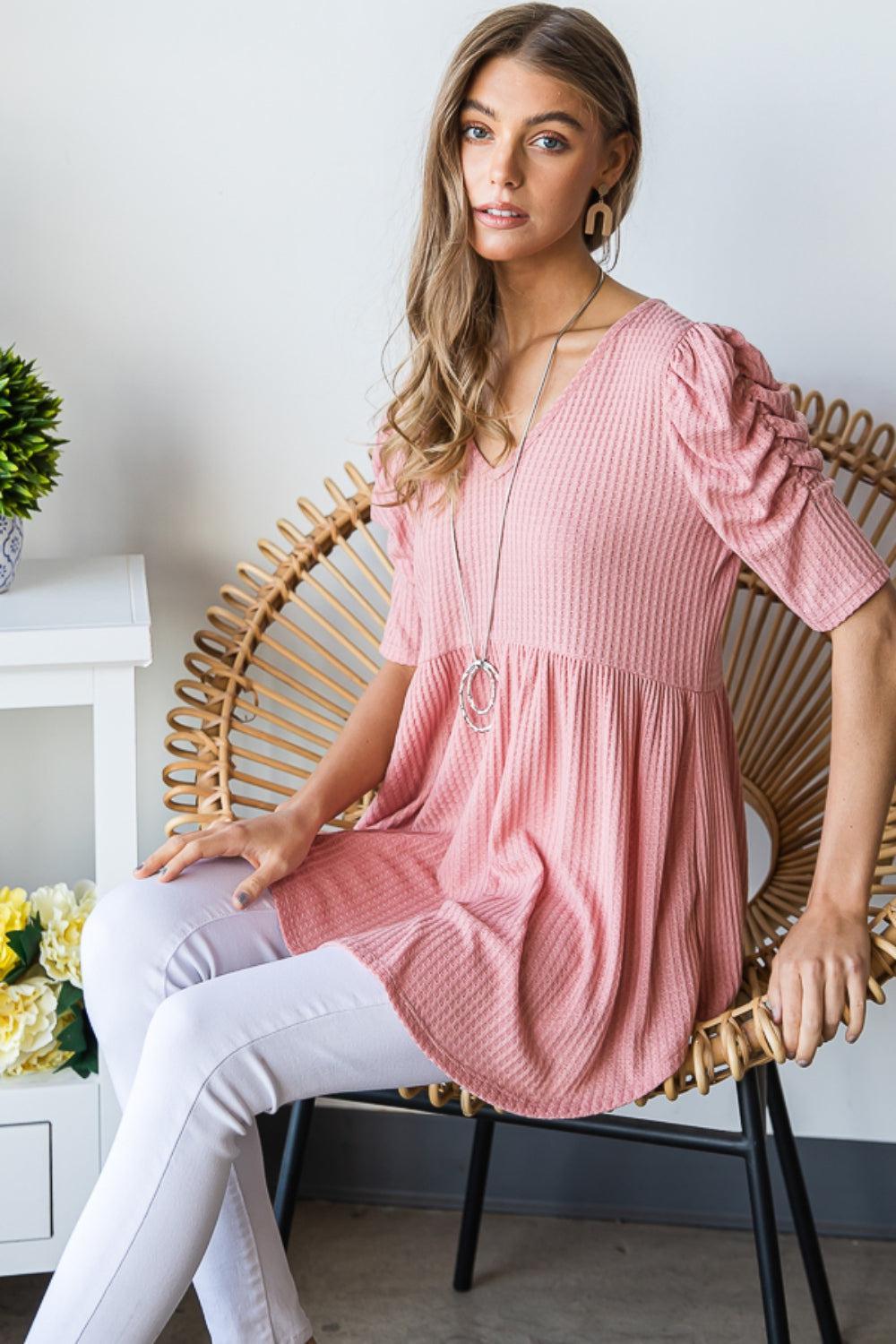 a woman sitting on a chair wearing a pink top