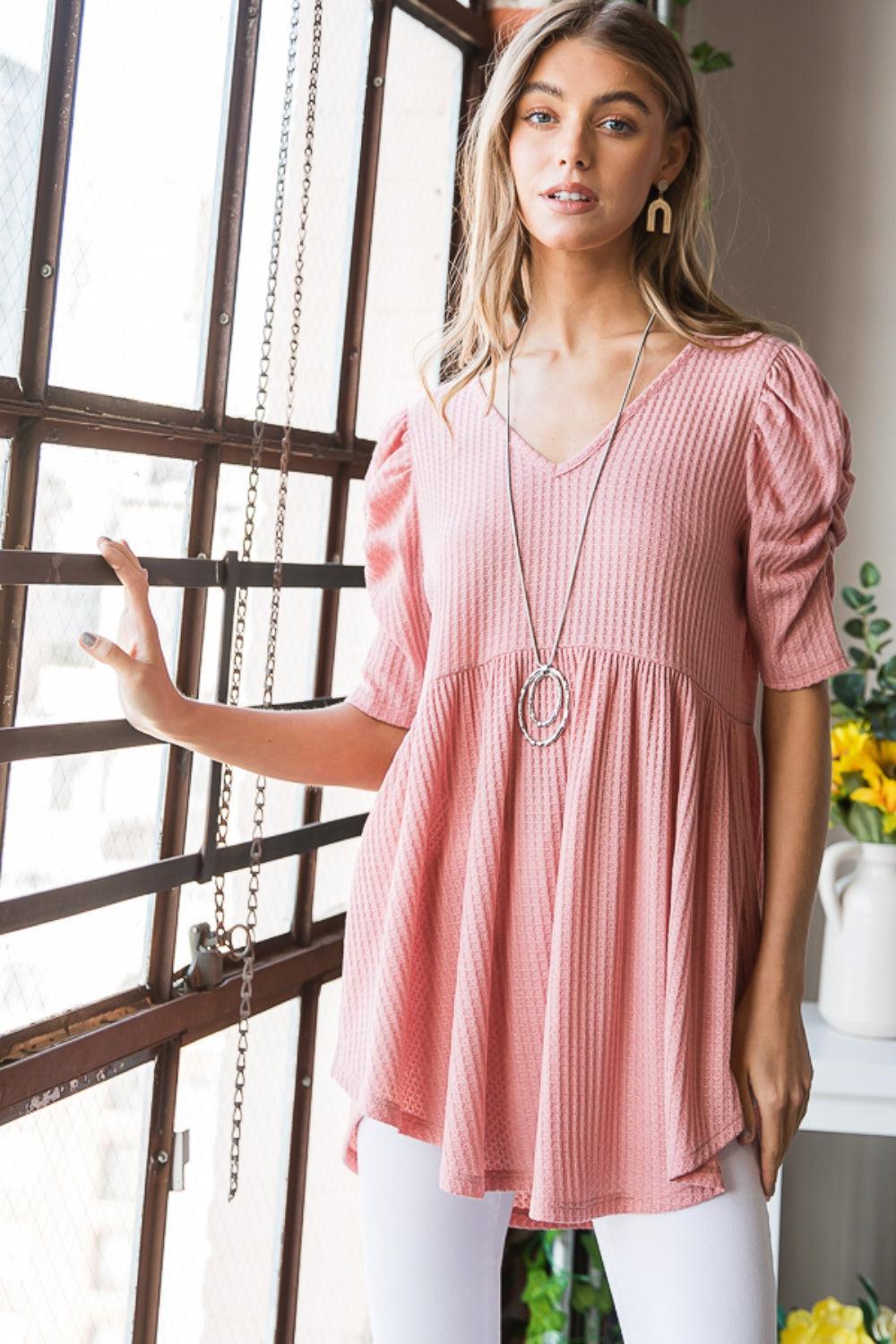 a woman standing in front of a window wearing a pink top