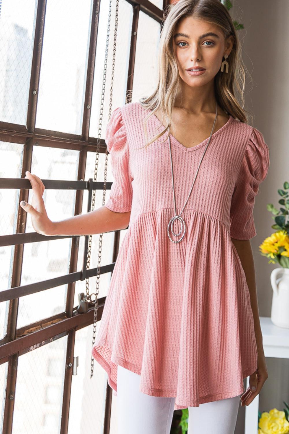 a woman standing in front of a window wearing a pink top