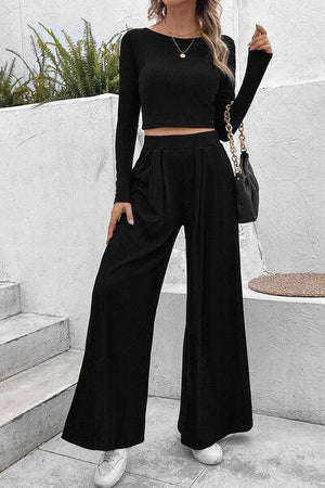 a woman wearing a black crop top and wide legged pants