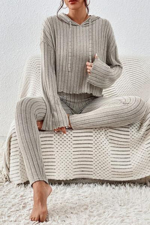 a woman sitting on a bed wearing a sweater and pants