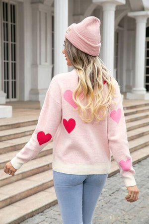 a woman wearing a pink heart sweater and jeans