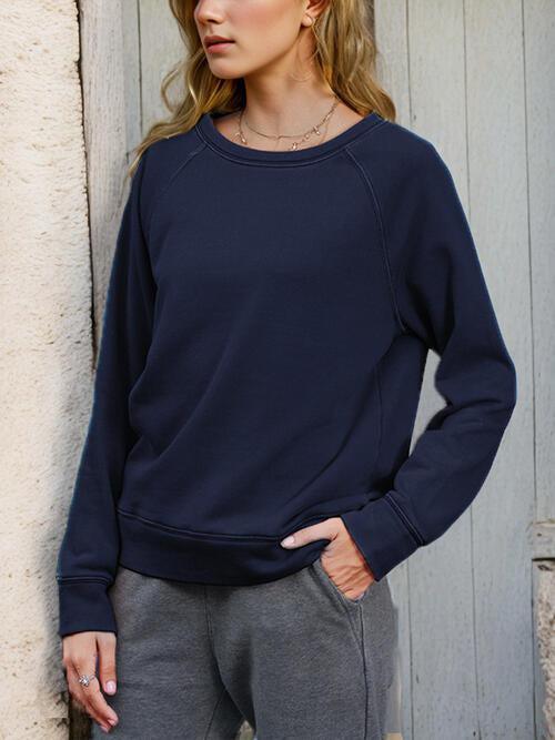a woman standing next to a wall wearing a blue sweatshirt
