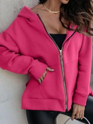 a woman leaning against a wall wearing a pink hoodie