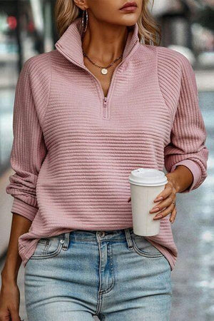 a woman holding a coffee cup and wearing a pink sweater