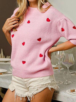 a woman wearing a pink sweater with hearts on it