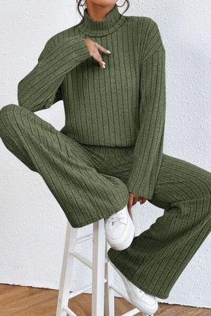 a woman sitting on a stool wearing a green sweater and pants