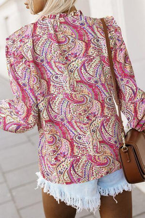 a woman wearing a pink paisley top and denim shorts