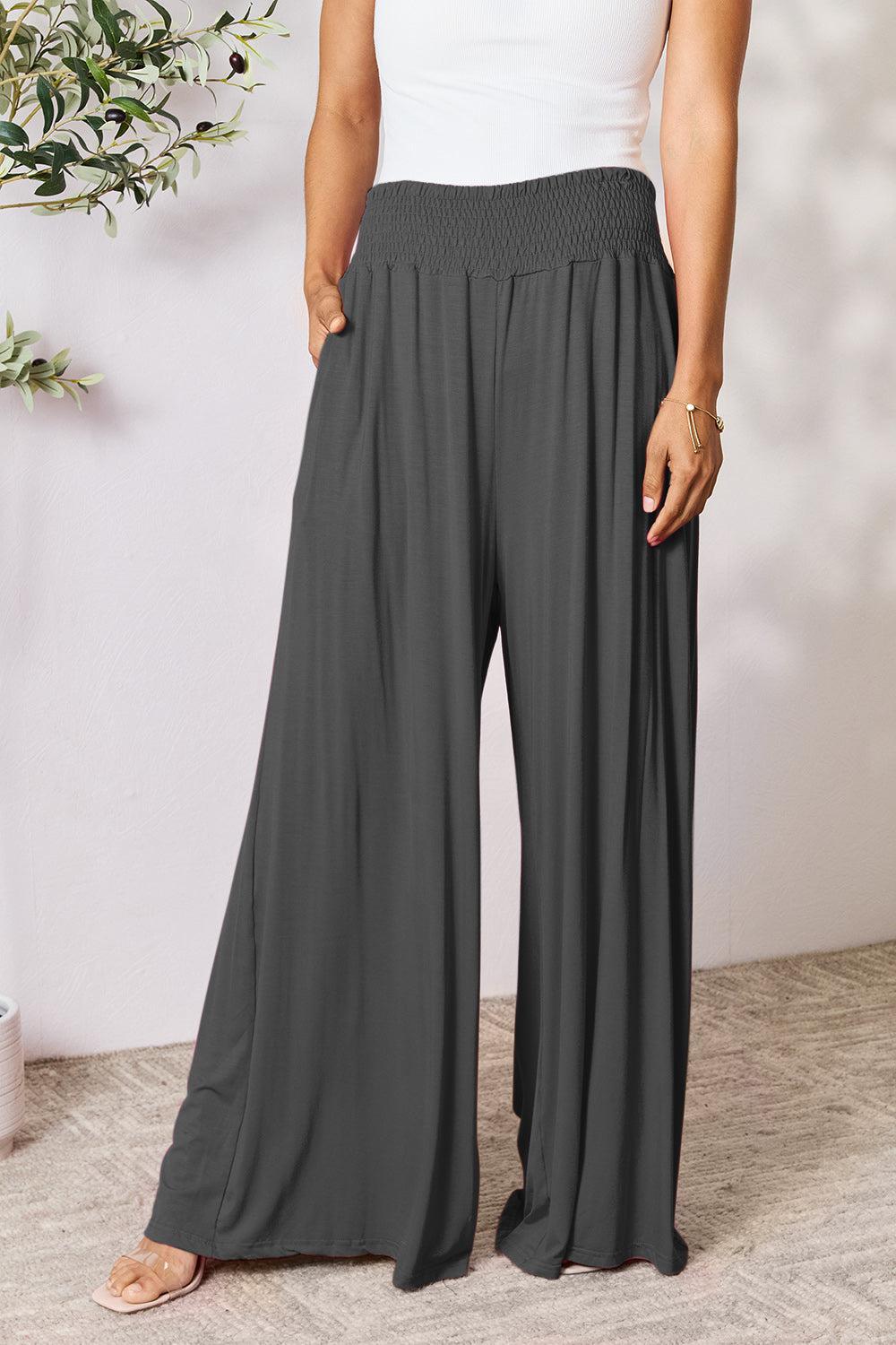 a woman wearing a white tank top and grey wide legged pants