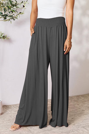 a woman wearing a white tank top and grey wide legged pants