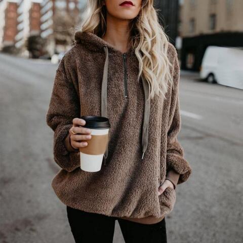 a blonde woman wearing a brown hoodie and black leggings holding a coffee