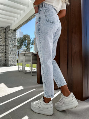 a woman in white shirt and jeans standing by a wall