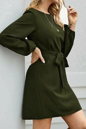 a woman leaning against a wall wearing a green dress