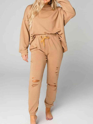 a woman wearing a tan sweatshirt and ripped pants