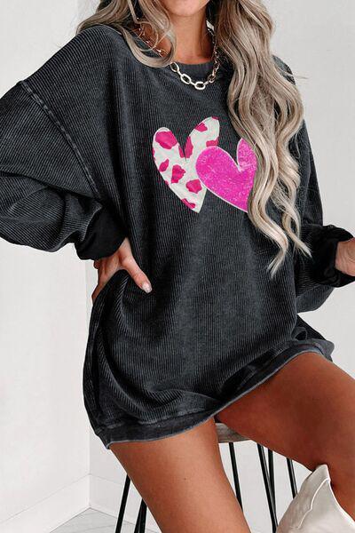 a woman sitting on a chair wearing a black sweater with a pink heart on it