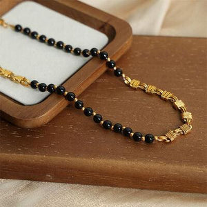 a black and gold beaded rosary on a wooden stand