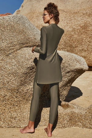 a woman in a gray suit standing in front of a rock