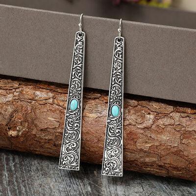 a pair of earrings sitting on top of a piece of wood