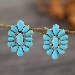 a pair of turquoise stone earrings hanging from a tree branch