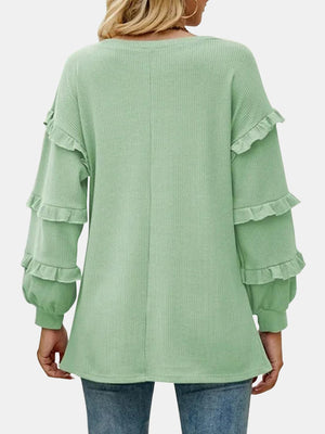 a woman wearing a green sweater with ruffled sleeves