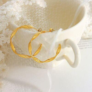 a pair of gold hoop earrings sitting on top of a white cup